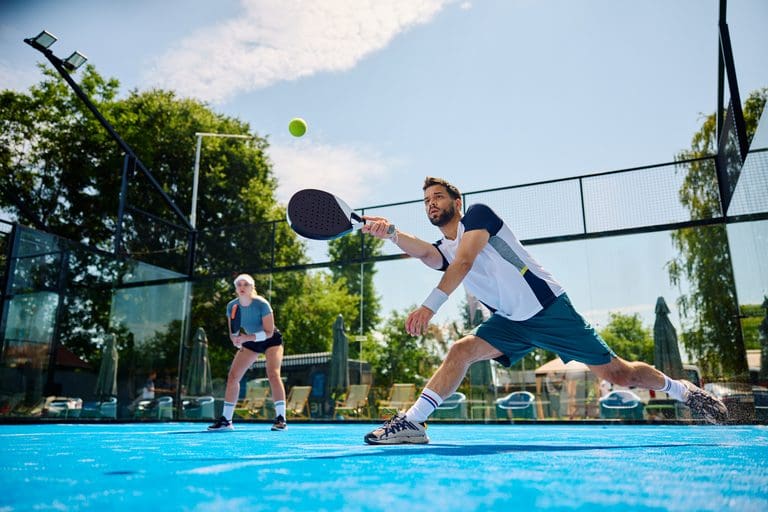 Paddle tennis player making an effort to while hitting the ball during a match on outdoor court